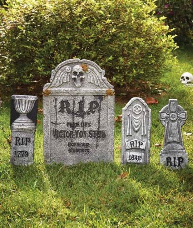 A set of four decorative gray Halloween tombstones arranged on green grass in front of bushes. The central main tombstone features a skull with wings and reads "R.I.P. Here Lies Victor Von Stein Born 1612 Died 1676." Click to shop all Halloween Graves.