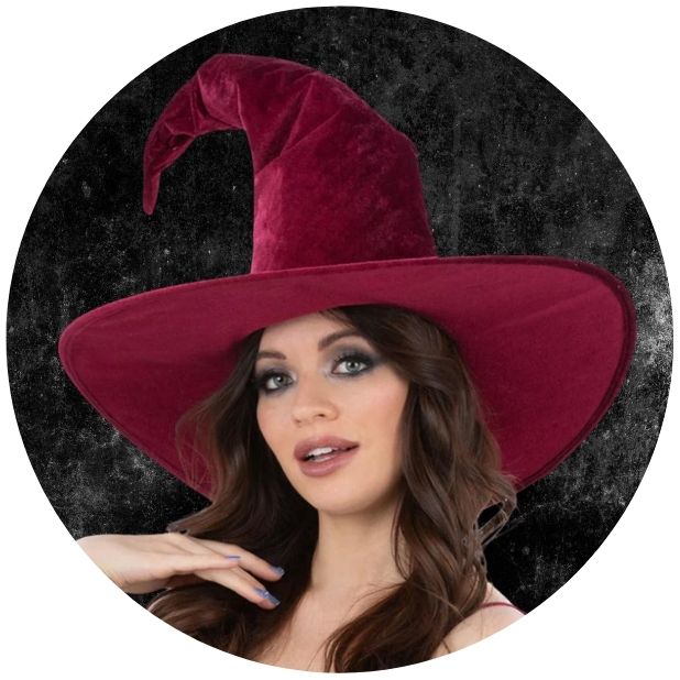 A black circle with a woman wearing a maroon velvet witch hat. Click to shop all Halloween hats and head wear.