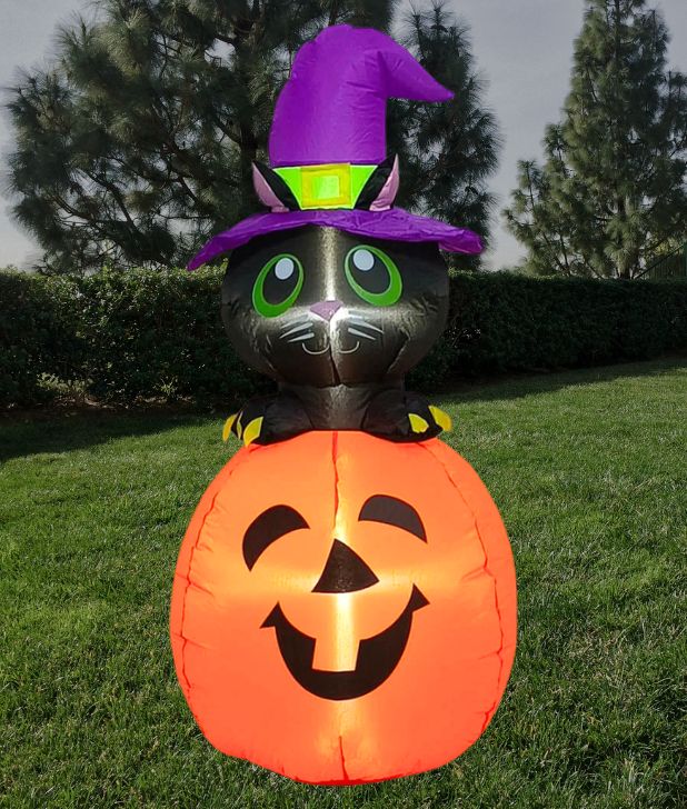 A grassy backyard with trees and a hedge and a halloween inflatable that is a pumpkin with a black cat wearing a purple witch hat. Click to shop all Family Friendly Halloween Decorations.