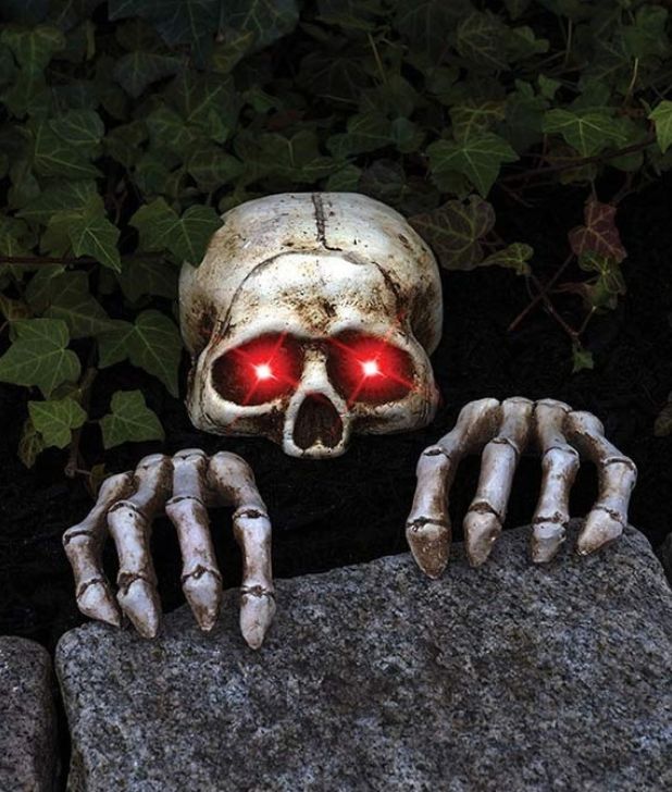 Halloween lawn decoration featuring a realistic skeleton skull with glowing red eyes and skeleton hands crawling over a stone border. Click to shop all Halloween Decorations.