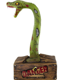 A green zombie snake animatronic decoration with a long curved neck, open mouth, red details, and a brown wood-textured base printed with a warning label reading 'DANGER UNDEAD SPECIMEN'.