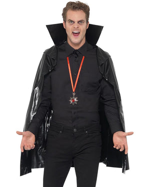 Person wearing a black vampire cape and costume with a red and silver medallion on a white background