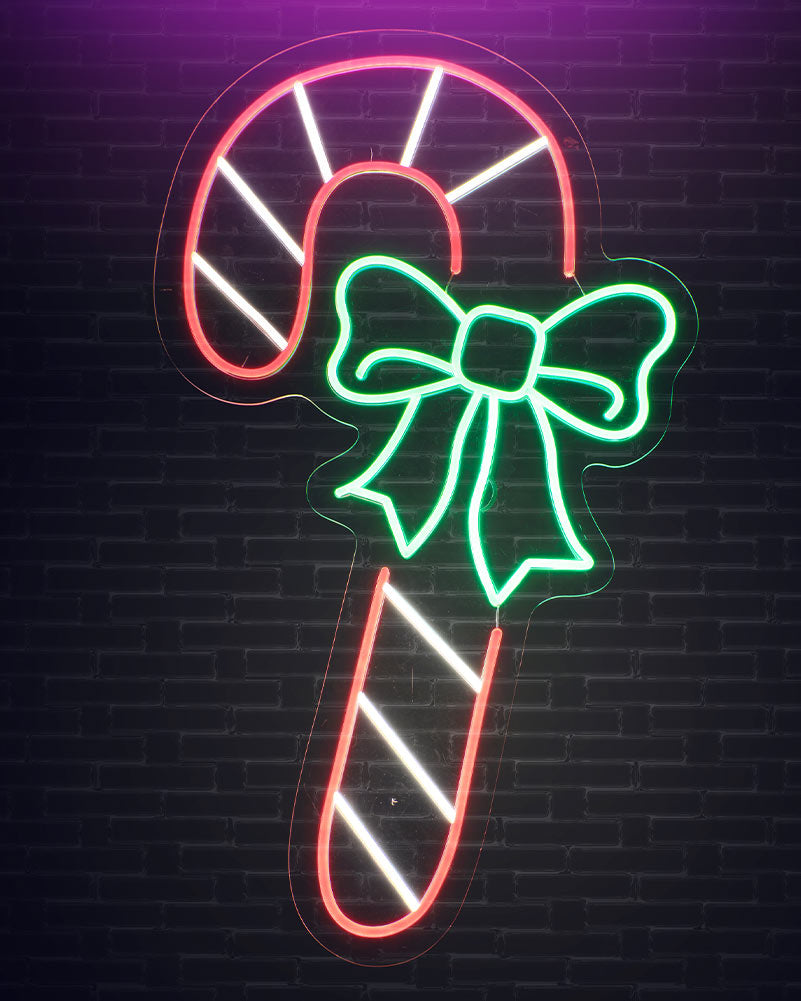 A neon sign shaped like a candy cane with a green bow, glowing against a dark brick wall background.