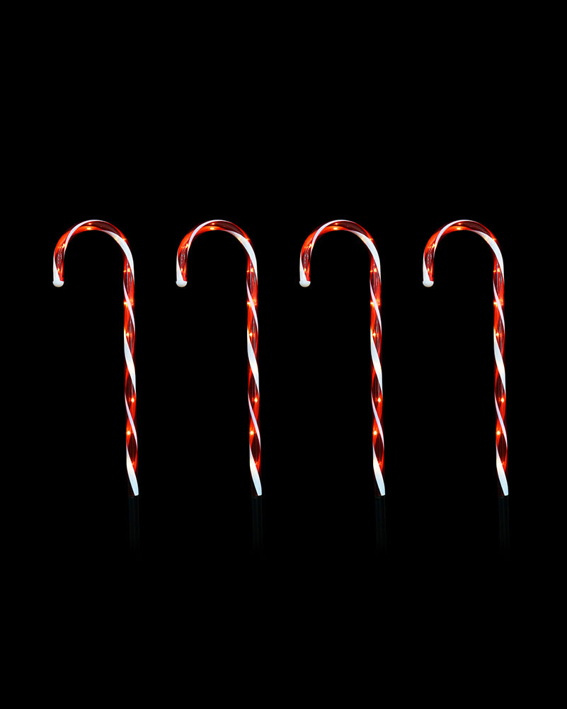 Four red and white striped candy canes arranged upright in a row against a solid black background.