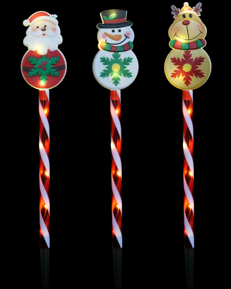 Three festive outdoor garden lights shaped like candy canes with holiday characters: Santa Claus, a snowman, and a reindeer, shown against a solid black background.