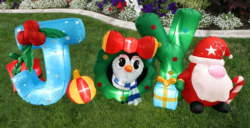 A grassy front yard with a Christmas Inflatable. It says "JOY" with a a mistletoe, presents, penguin and a Santa. Click to shop all Christmas Lawn Inflatables. 