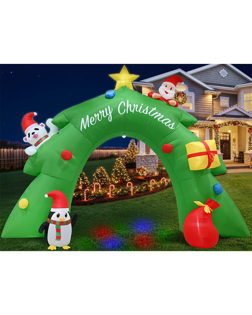 Green inflatable Christmas tree arch decoration with white 'Merry Christmas' script, decorated with colorful ornaments, a penguin, Santa, and gift graphics, shown set up on a lawn in front of a house at night.
