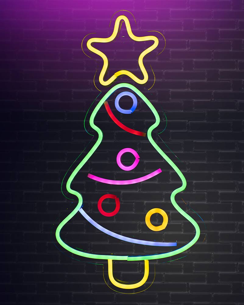 A neon Christmas tree sign with a yellow star on top, glowing multicolor lights, set against a dark brick wall background.