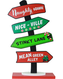 A Christmas-themed directional signpost with four arrow-shaped signs pointing to 'Naughty Square', 'Nice - Ville', 'Stinky Lane', and 'Mean Green Alley' on a black pole with a red and white base, shown on a white background.