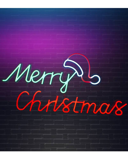 A neon sign reading 'Merry Christmas' with a Santa hat outline, mounted on a dark brick wall. The letters glow in mint green and red, with the hat outlined in white and red.