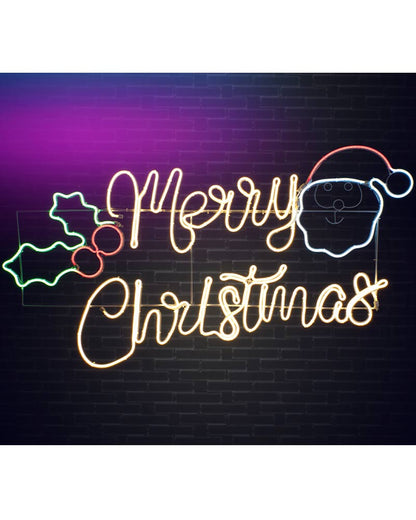 A glowing Christmas neon sign on a dark brick wall background, featuring the words “Merry Christmas” in warm yellow script, a Santa face outline in blue and white, and holly leaves in green and red.