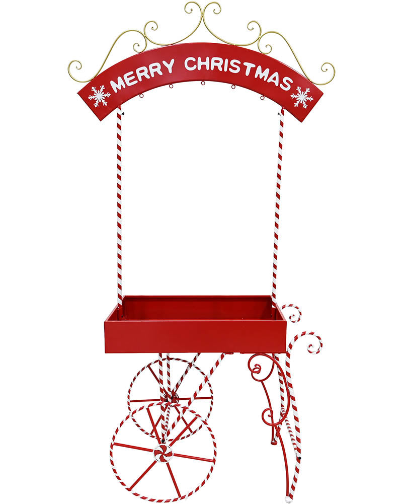 A red metal Christmas market stall decoration with a 'MERRY CHRISTMAS' arched sign, hanging rope supports, a tray, and decorative wheel and cane details on a white background.