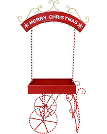 A red metal Christmas market stall decoration with a 'MERRY CHRISTMAS' arched sign, hanging rope supports, a tray, and decorative wheel and cane details on a white background.