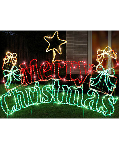 Outdoor Christmas yard sign with illuminated red 'Merry' lettering, green 'Christmas' lettering, gift boxes with bows, and a glowing star on a lawn at night.