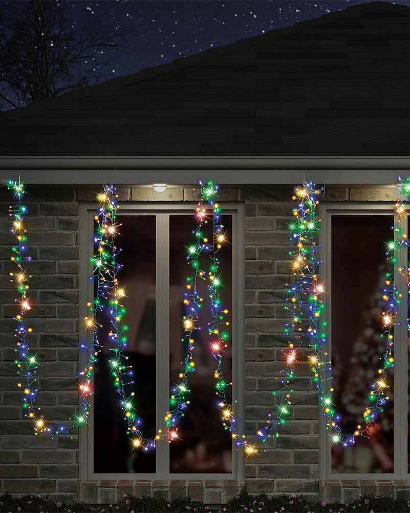 Multicolor Christmas string lights draped vertically across the windows of a brick house at night under a starry sky.