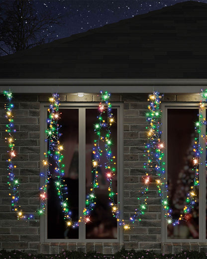Multicolor Christmas string lights draped vertically across the windows of a brick house at night under a starry sky.
