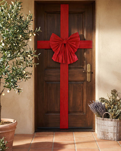 A dark brown wooden front door decorated with a large red fabric bow and matching red ribbon running vertically down the center, shown in a warm beige entryway with potted plants and terracotta tile flooring.