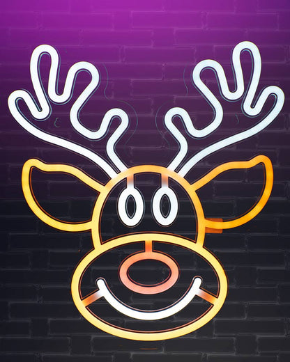 A neon-style reindeer face sign with white antlers and eyes, yellow ears and nose outline, and a pink nose, set against a purple-to-black brick wall background.