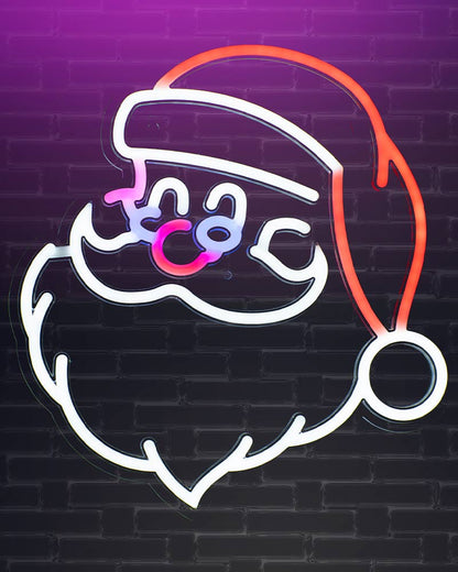 A neon sign depicting a stylized Santa Claus face and hat, glowing with white, pink, purple, and orange light against a dark brick wall background.