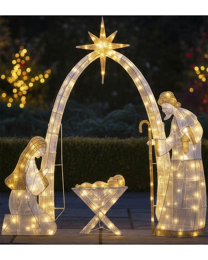 Outdoor Christmas light nativity scene with illuminated figures of Mary, Joseph, and baby Jesus under a glowing star arch, set against a dark garden background at night.