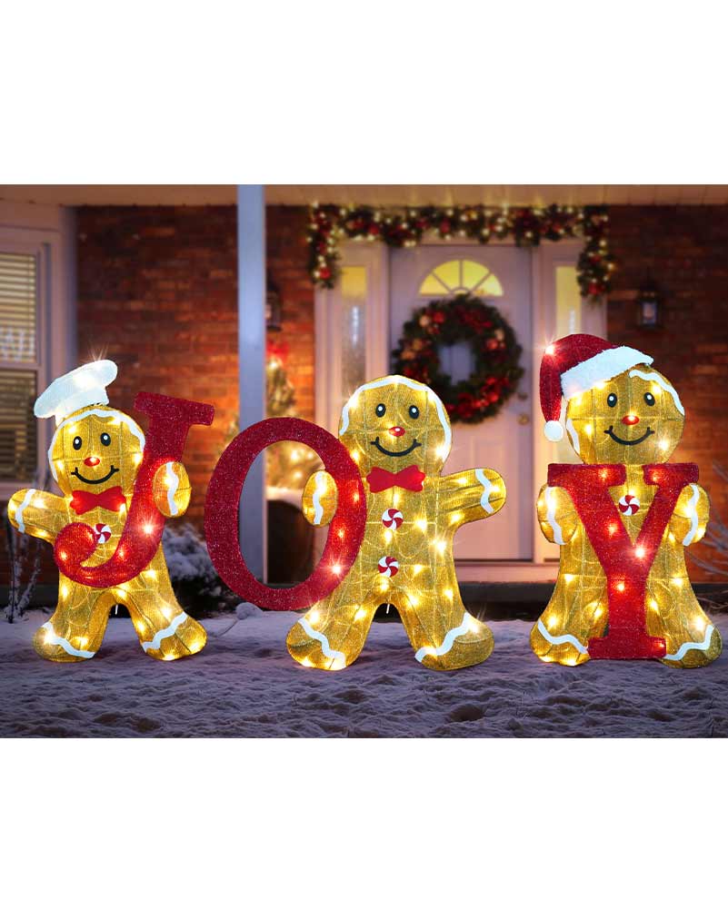 Three gingerbread man holiday light decorations spelling JOY in front of a decorated house door at night.