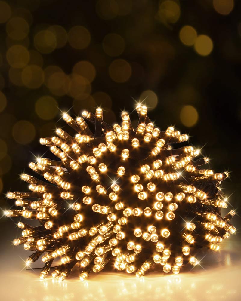 A cluster of warm white LED fairy string lights glowing brightly, photographed against a dark, softly blurred bokeh background with golden light reflections.