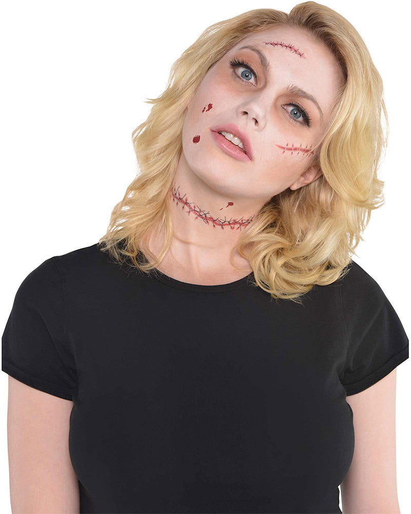 A blonde woman wearing a black short-sleeve t-shirt and fake stitched tattoos on her neck and face, posed against a solid white background.