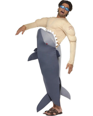 A person wearing a Man-Eating Shark Men's Costume, which includes a full-body shark jumpsuit with a human torso rising out of a shark's mouth, grey shark features sharp white teeth and red eyes, and blue goggles with specs.